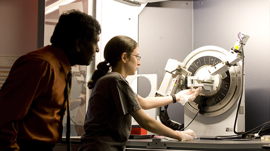 Student works with a device in the optics lab as professor looks on.